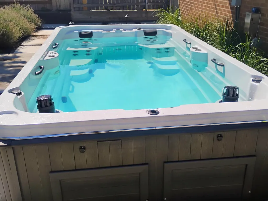 Hot tub with clear, still water beside a brick house in a fenced backyard