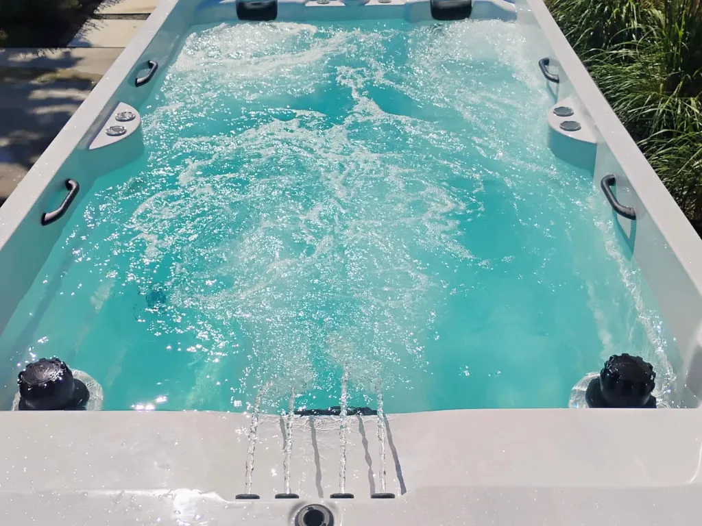 Long hot tub with the jets running and clear blue water in a fenced backyard