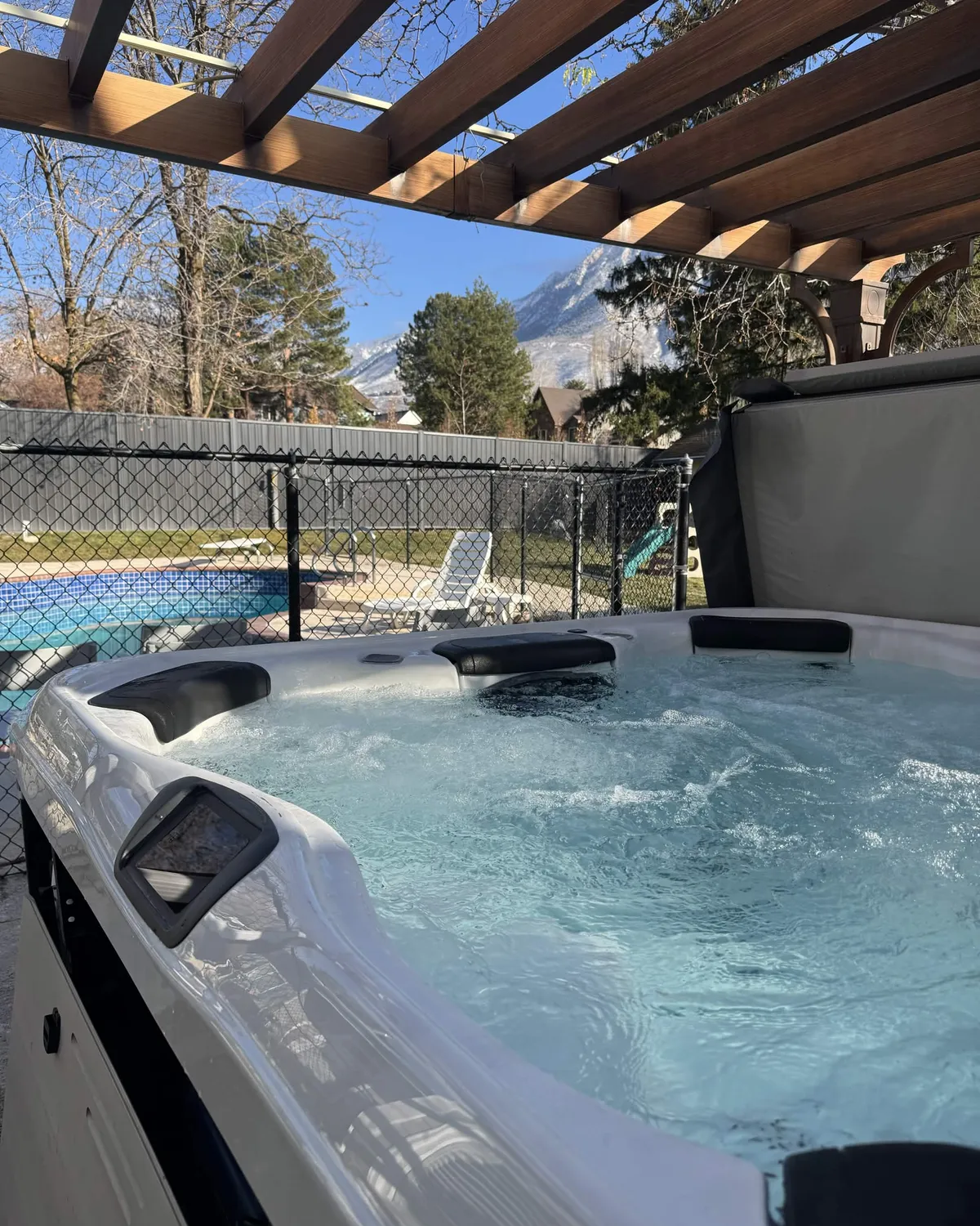 Hot tub running under a wood pergola in a Salt Lake Valley backyard with the snow-capped Wasatch mountains behind